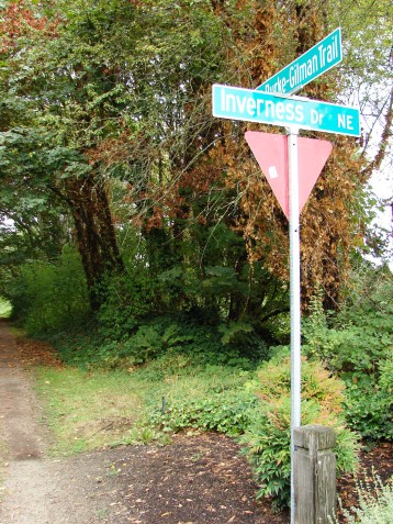 Looking north on the Burke Gilman Trail where it crosses the entrance driveway to Inverness. In the time that I stood watching bicyclists on the Trail, none slowed down to see whether any cars were coming across.