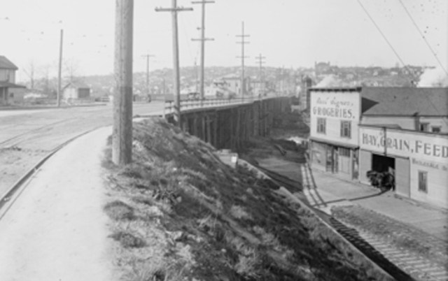 Carl Signor's grocery store is seen in this 1915 photo looking north. The posts of the trestle bridge to Fremont can be seen. On the horizon is B.F. Day School. Photo 2787, Seattle Municipal Archives.